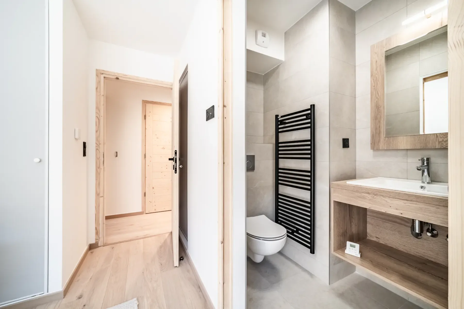 A bathroom with a toilet, wall-mounted towel warmer, and wood-toned vanity.