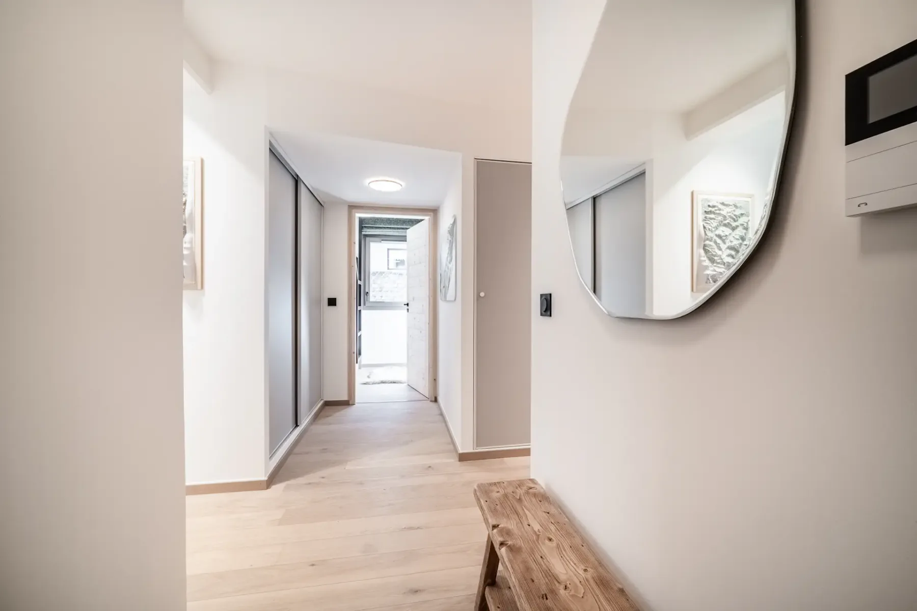 A bright hallway with pale wood flooring leads to a glass entry door.