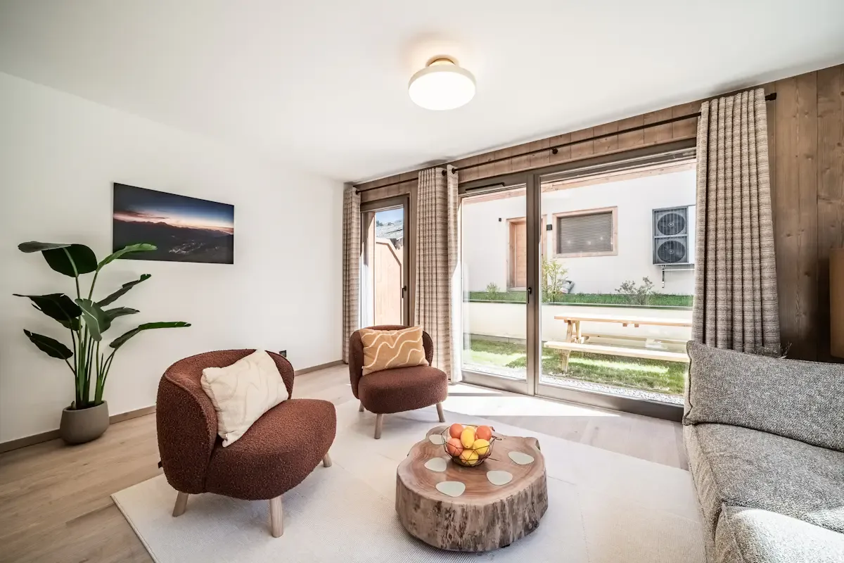 A bright living room with seating beside large windows opening onto a patio.