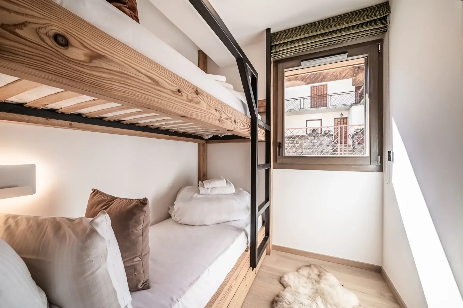 A compact sleeping area with wooden bunk beds, white bedding, and a window.