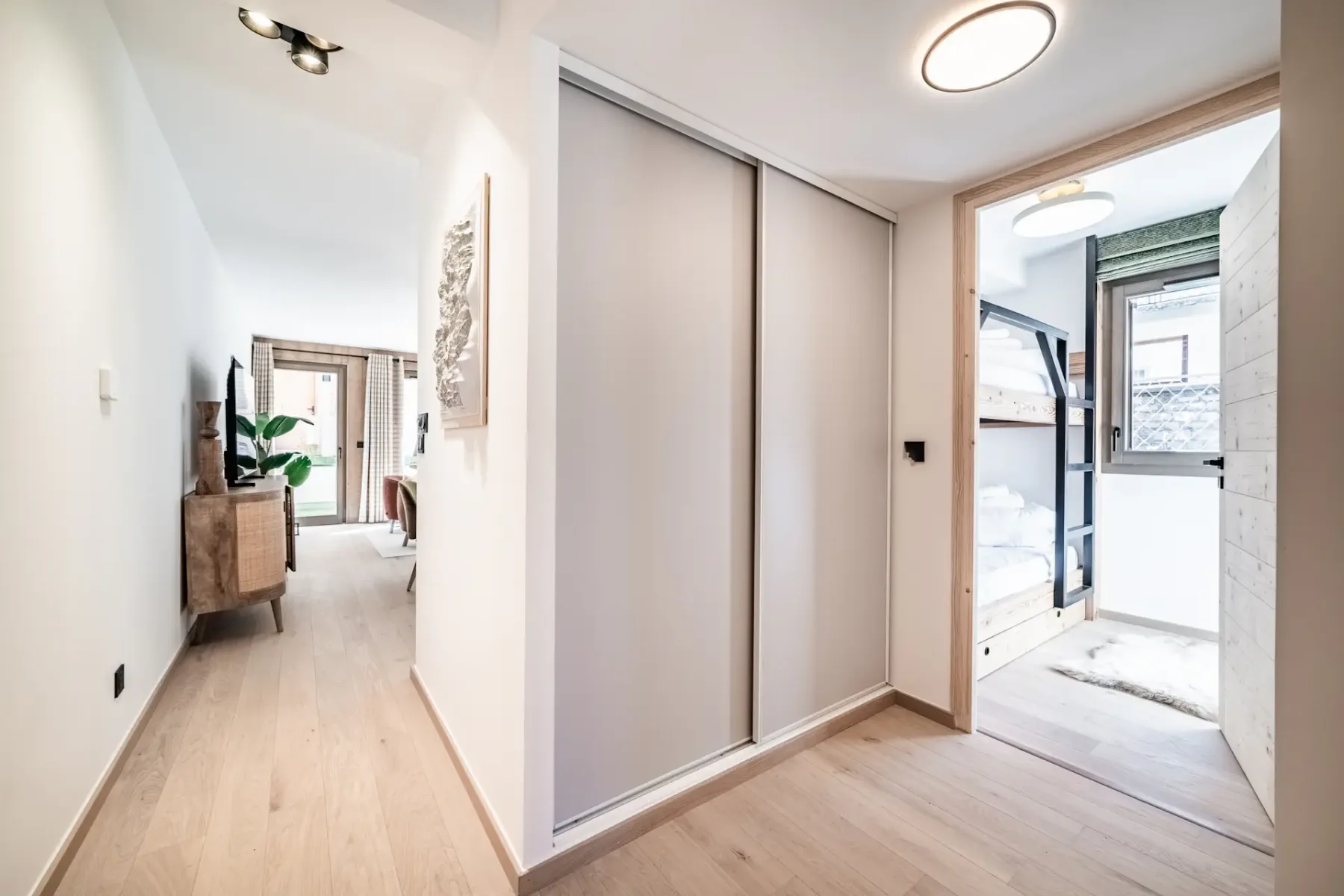 A bright hallway with light wood flooring and a room with bunk beds visible through an open doorway.