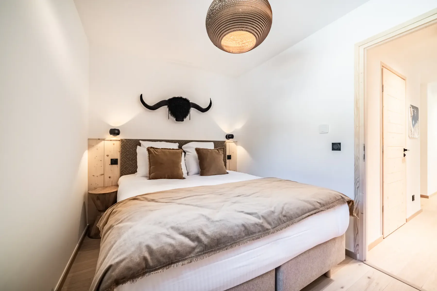 Cozy bedroom with a large bed, brown and white bedding, bull head wall decor, and a woven ceiling light, creating a warm and inviting atmosphere.