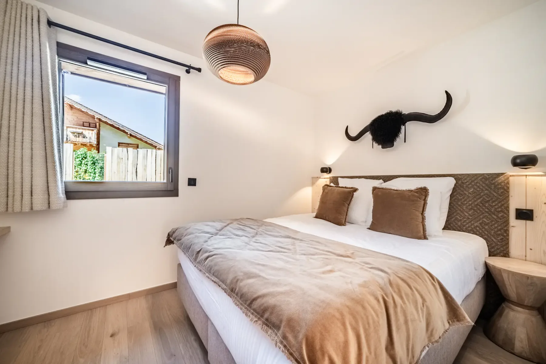 Cozy bedroom with a large bed, brown and white bedding, bull head wall decor, and a woven ceiling light, creating a warm and inviting atmosphere.