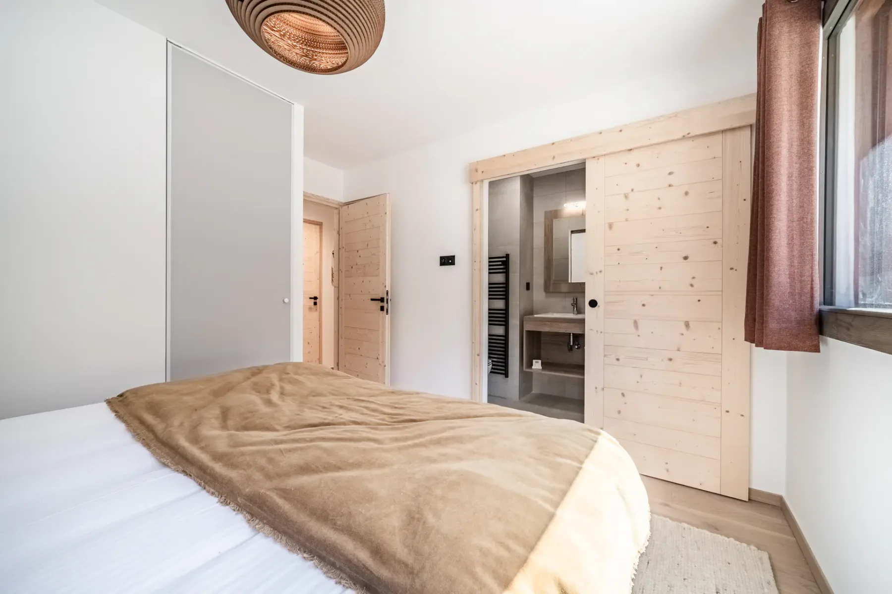 Bedroom with a bed, a brown blanket, and light wood doors.