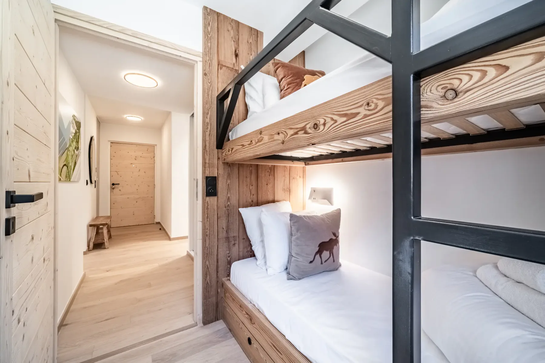 A bedroom with wooden bunk beds and white bedding beside a hallway.