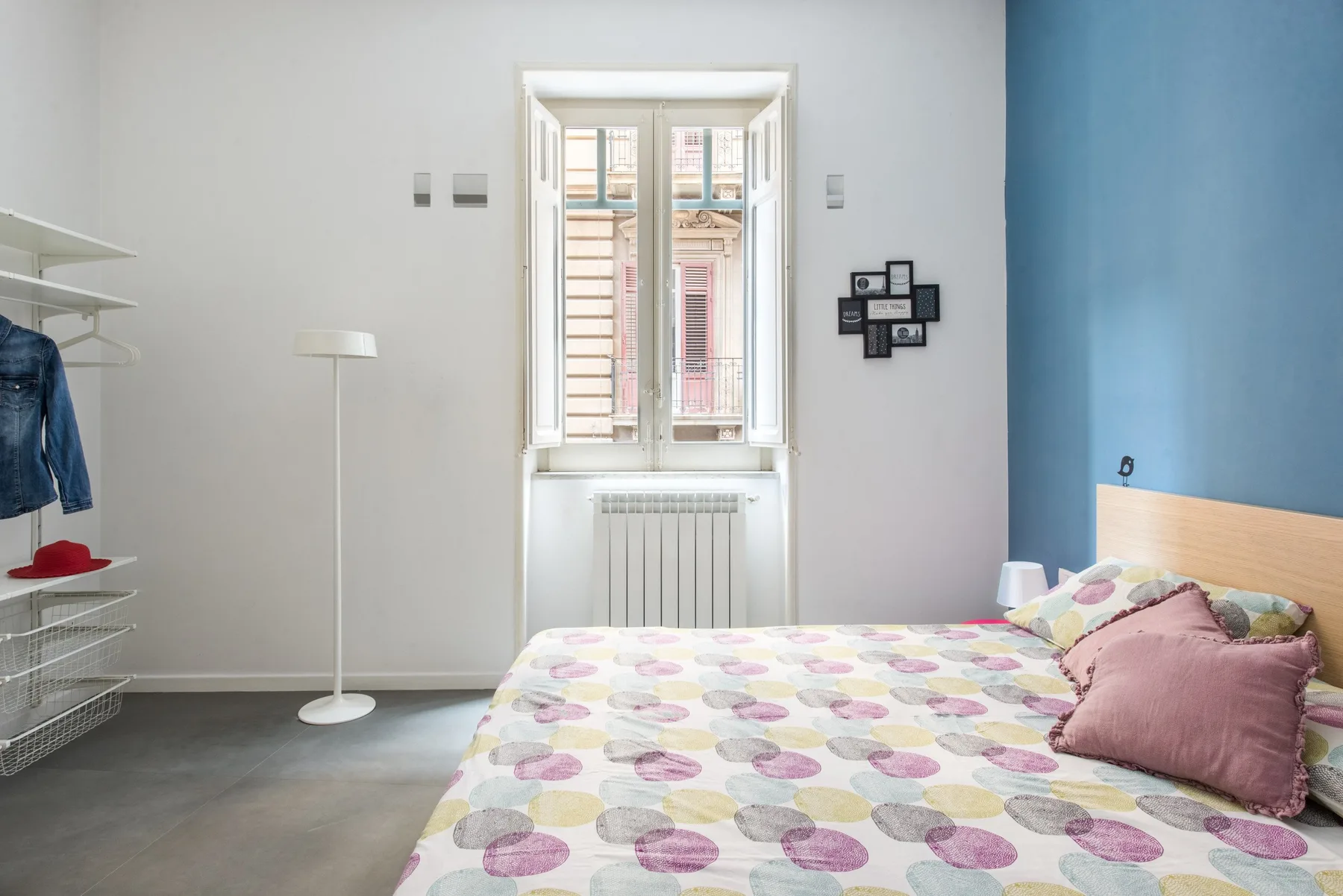 A bedroom with a patterned bed beside a window and blue accent wall.