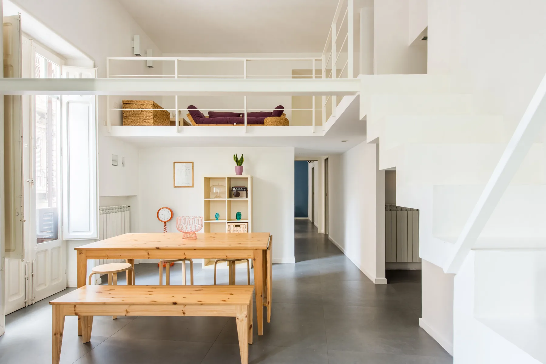 A bright open-plan dining area with a wooden table beneath a lofted seating space.