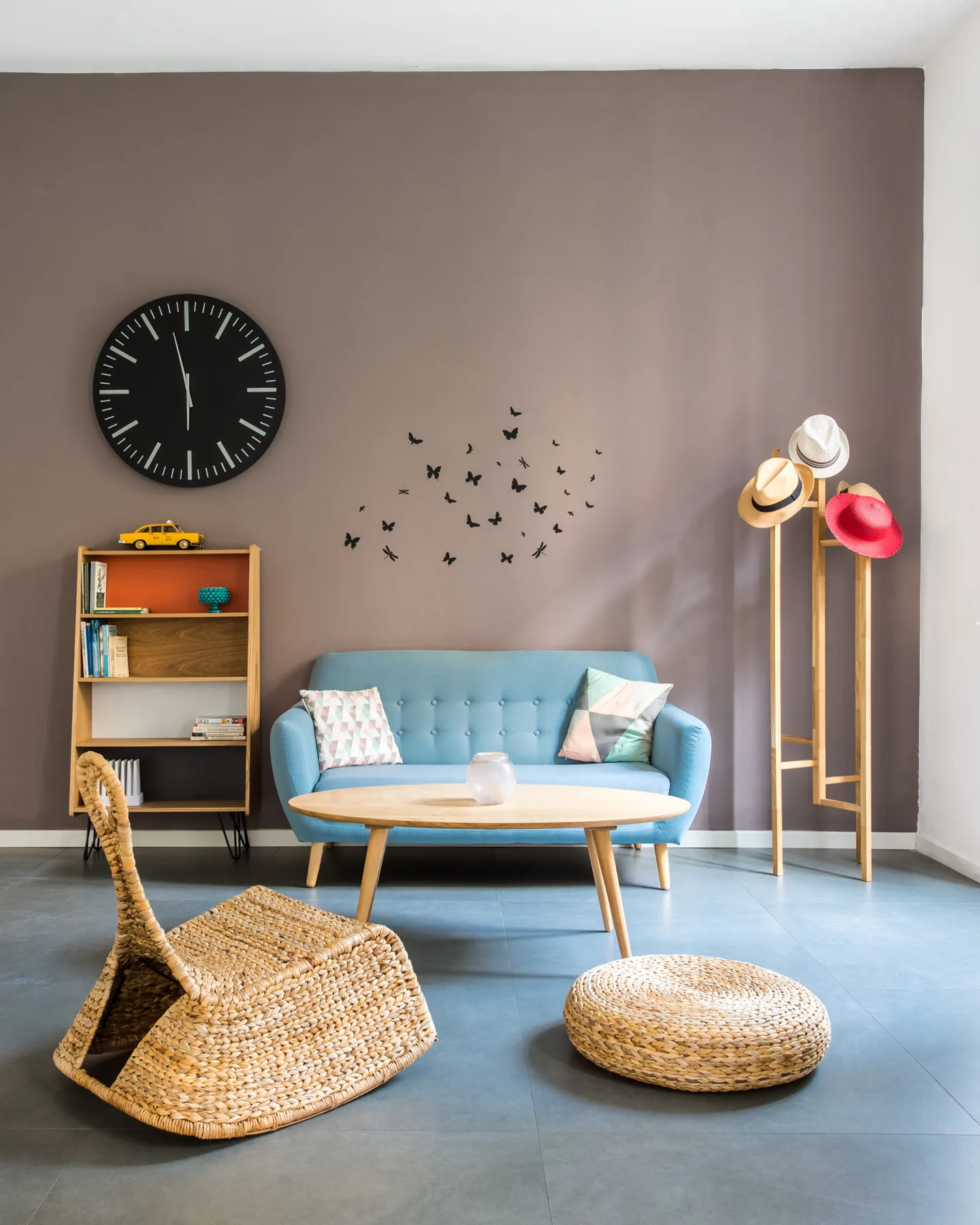 A living room with a blue loveseat, a wall clock, and woven seating.