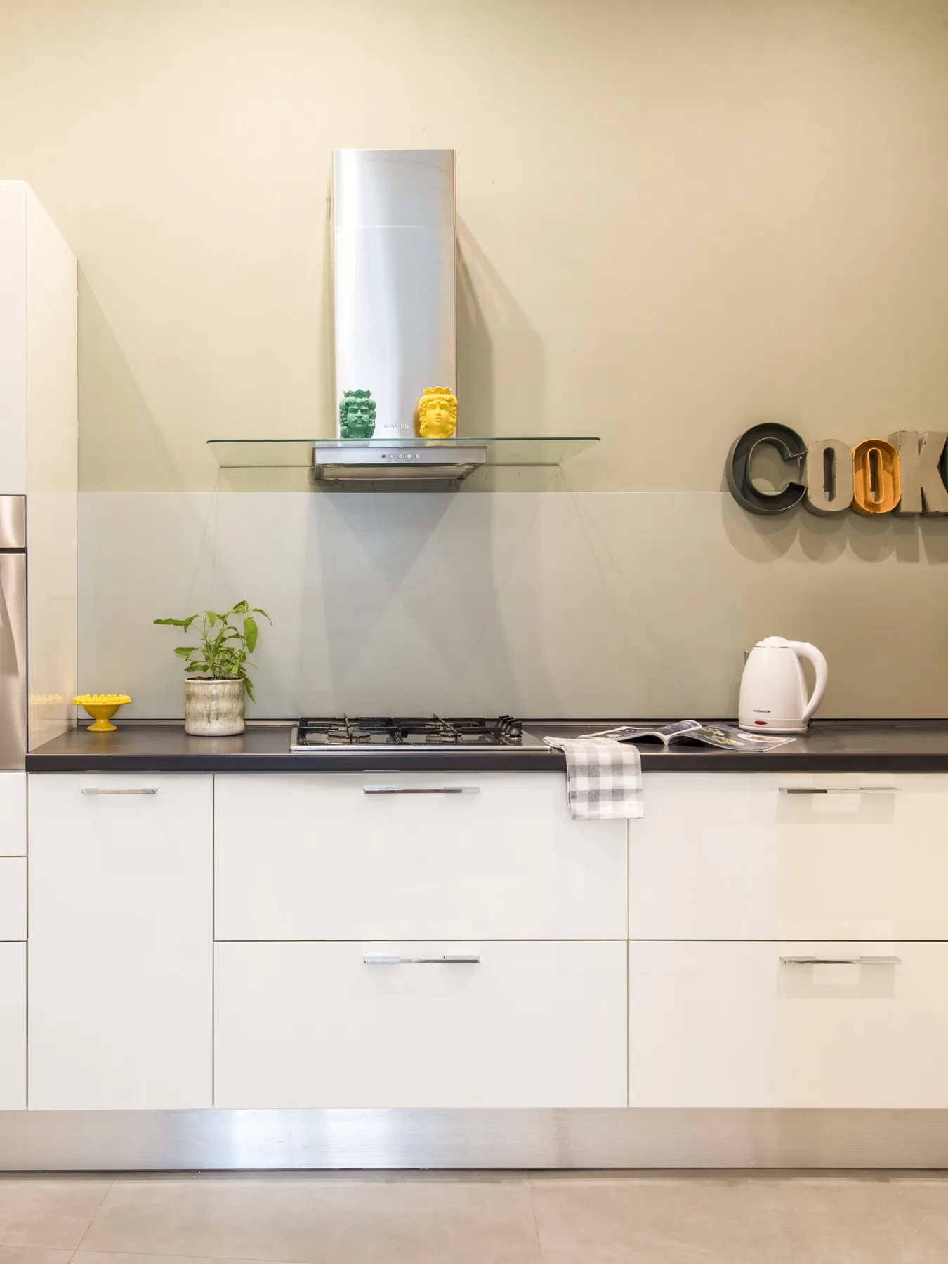 A modern kitchen with white cabinets, a cooktop, and countertop appliances.