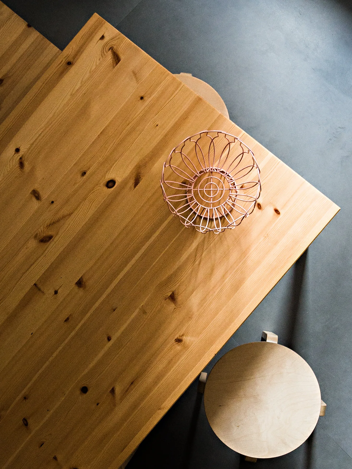 A wooden table with a wire basket sits beside a round stool.
