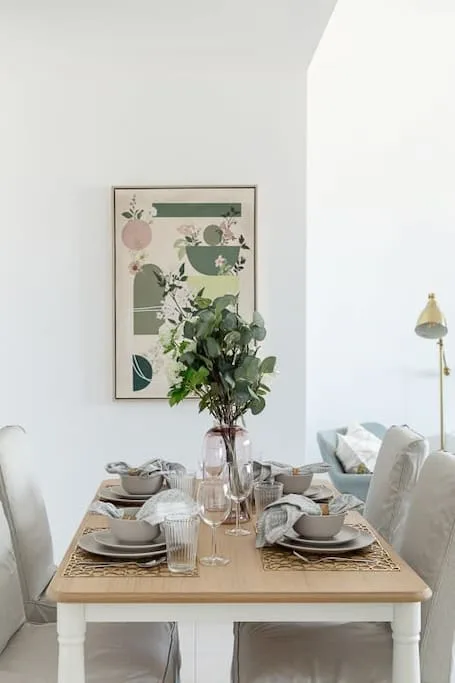 Una mesa de comedor está puesta con platos y vasos en una habitación luminosa.