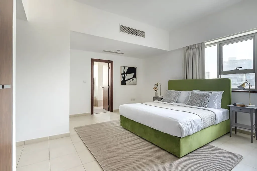 Un dormitorio luminoso con una cama verde junto a grandes ventanas.