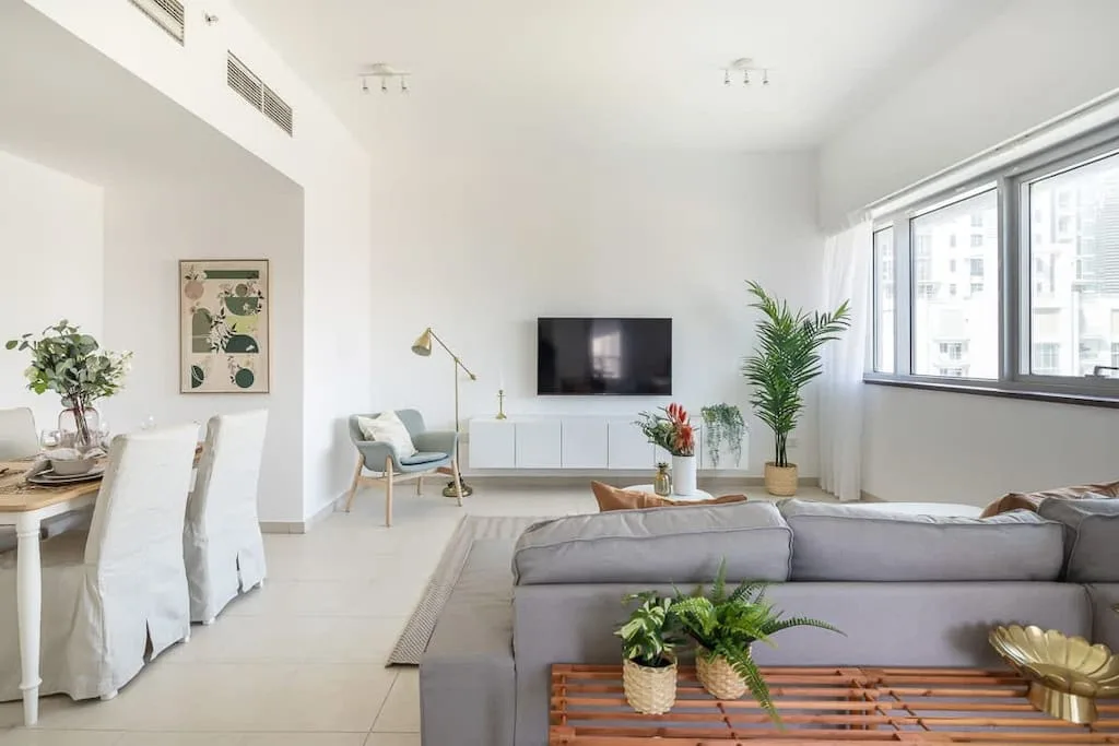 Una luminosa sala de estar y comedor con televisor, asientos y grandes ventanas.