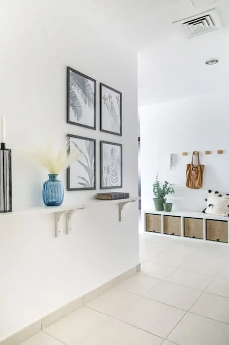 Un interior blanco y luminoso con láminas botánicas enmarcadas y un estante junto a un banco.
