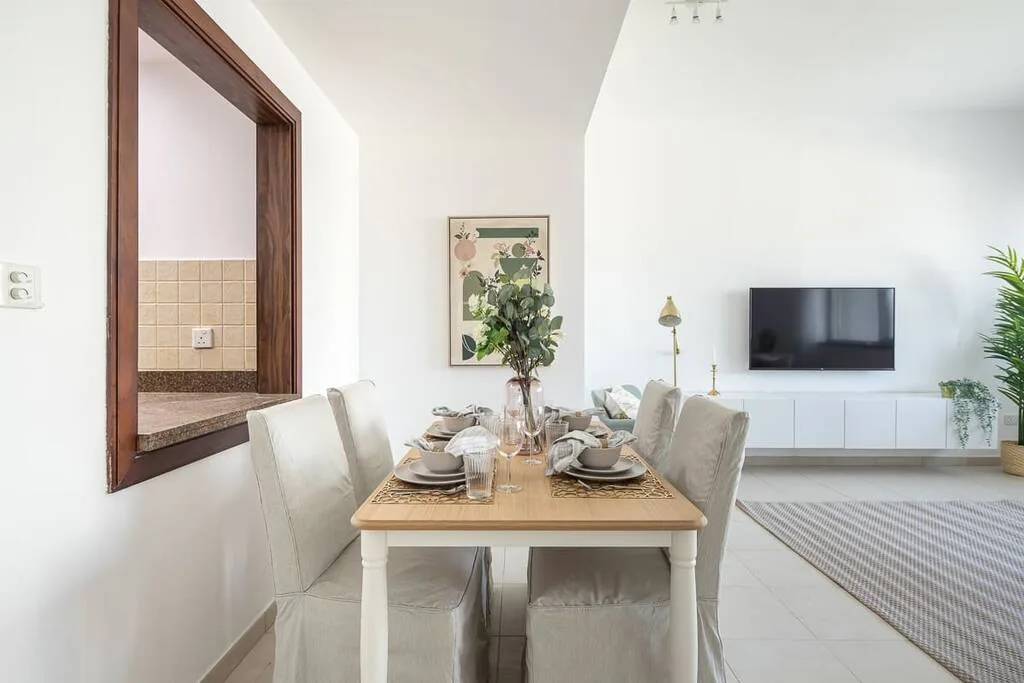 Un comedor con la mesa puesta, junto a una sala de estar con televisor.