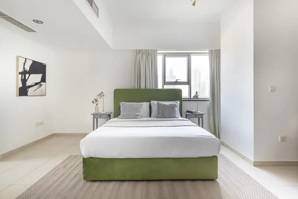 Un dormitorio luminoso con una cama verde frente a una ventana.
