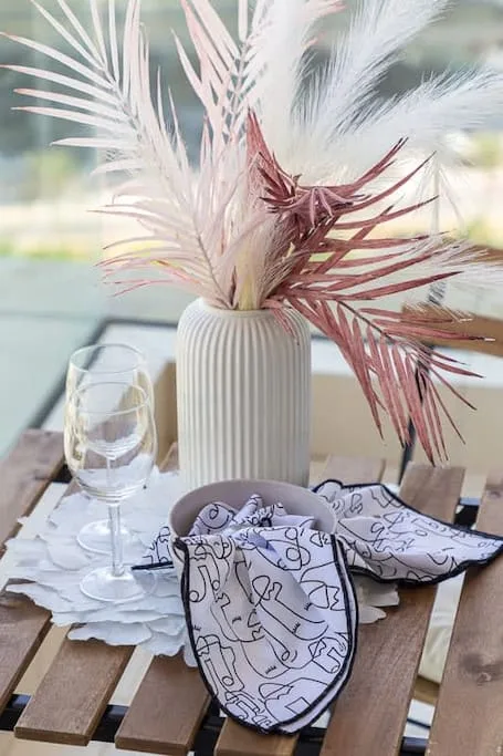 Una mesa está puesta con un jarrón de follaje seco, una copa y servilletas estampadas.