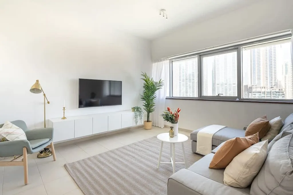 Una sala luminosa con asientos, un televisor y grandes ventanas.