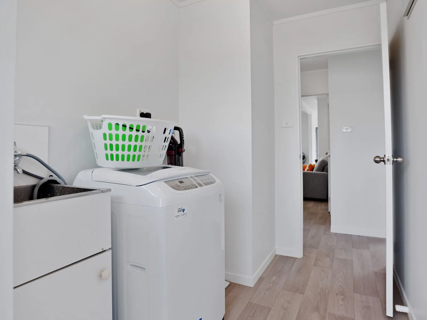 Un cuarto de lavado con una lavadora, una cesta para la ropa, un fregadero y una puerta que da a otra habitación en A Wave From It All - Waihi Beach Holiday Home Waihi Beach