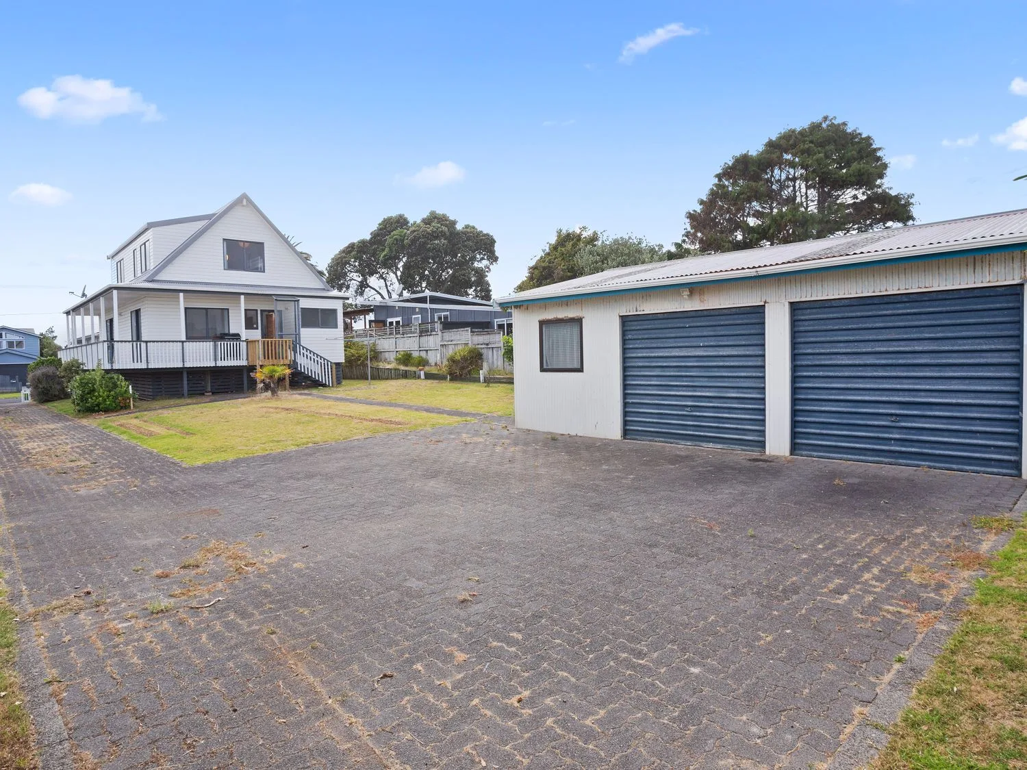 Una casa con un porche que la rodea y un garaje para dos coches con puertas azules en una zona residencial en A Wave From It All - Waihi Beach