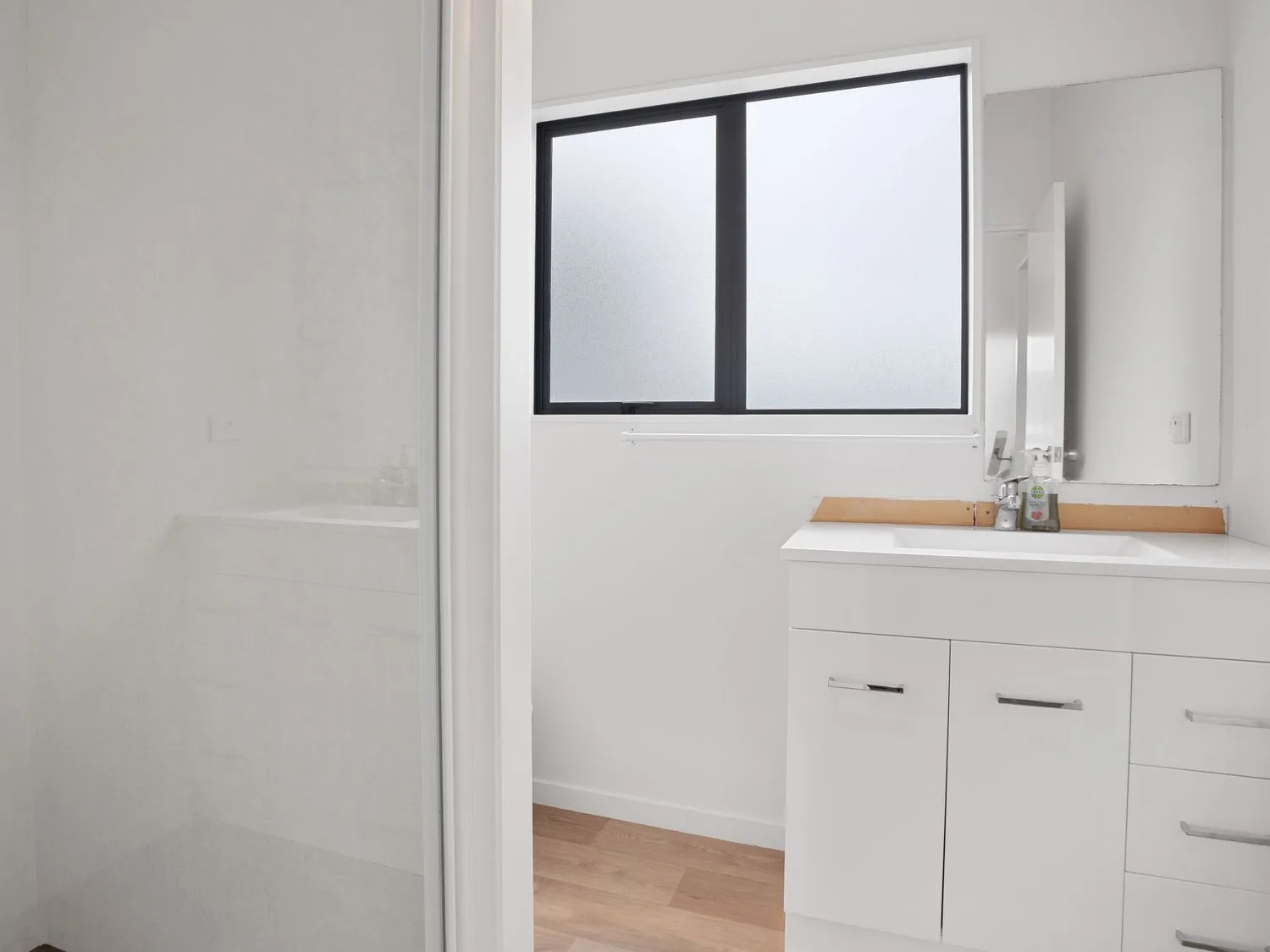 Un baño luminoso con un mueble blanco, espejo y ventana esmerilada.