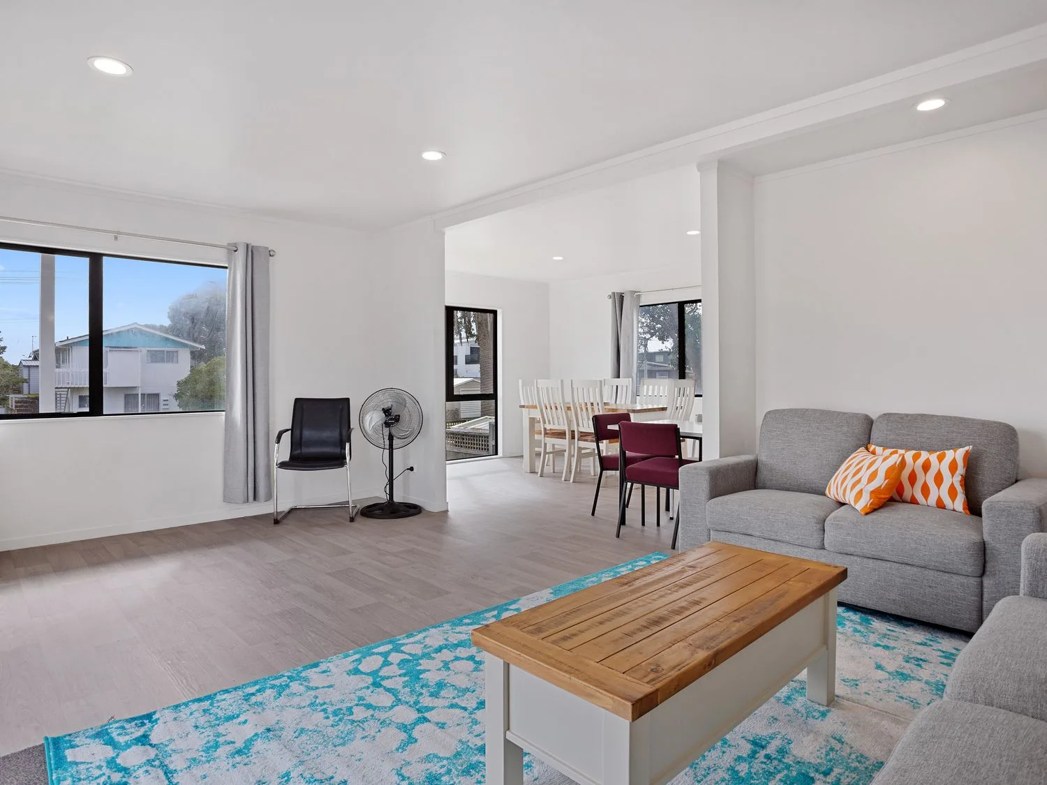 A bright living area has gray seating beside a wooden coffee table and blue patterned rug.