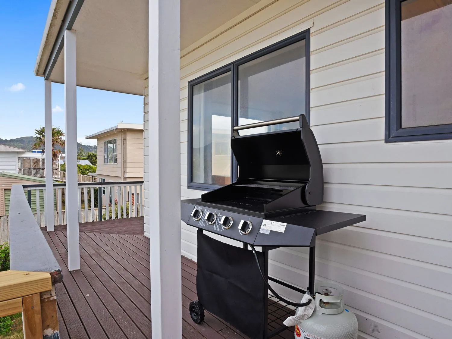Una terraza de madera con una barbacoa de gas y una barandilla en A Wave From It All - Waihi Beach Holiday Home Waihi Beach