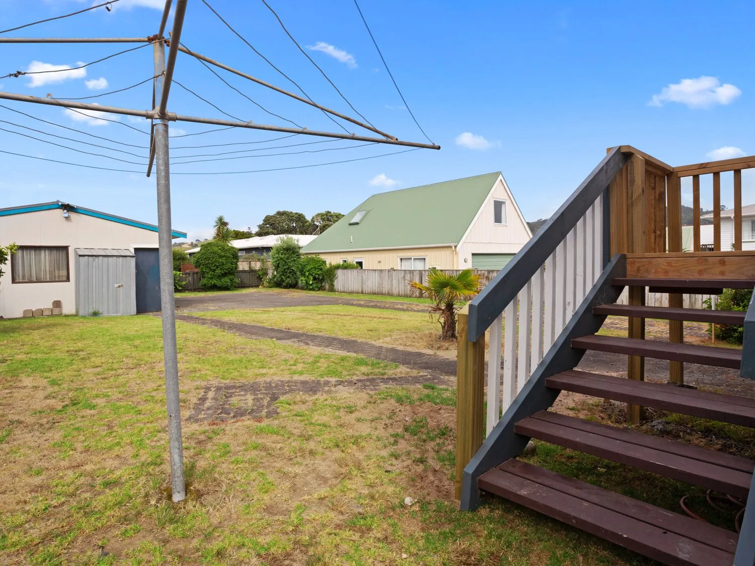 Un patio trasero con un tendedero giratorio, una escalera de madera y una pequeña caseta en A Wave From It All - Waihi Beach Holiday Home, en Waihi Beach