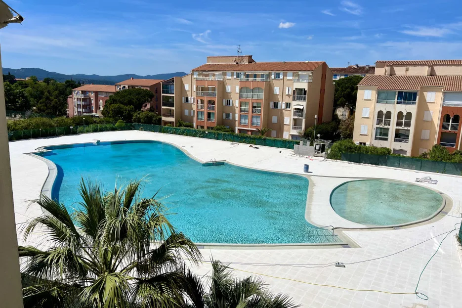 An outdoor swimming pool beside apartment buildings, with a smaller round pool nearby.