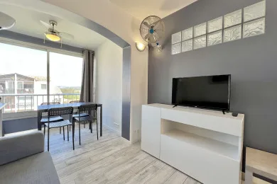 A bright living room with a dining table beside large windows and a television.