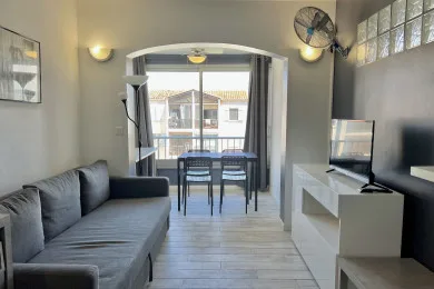 A living room with seating and a dining table beside large windows.