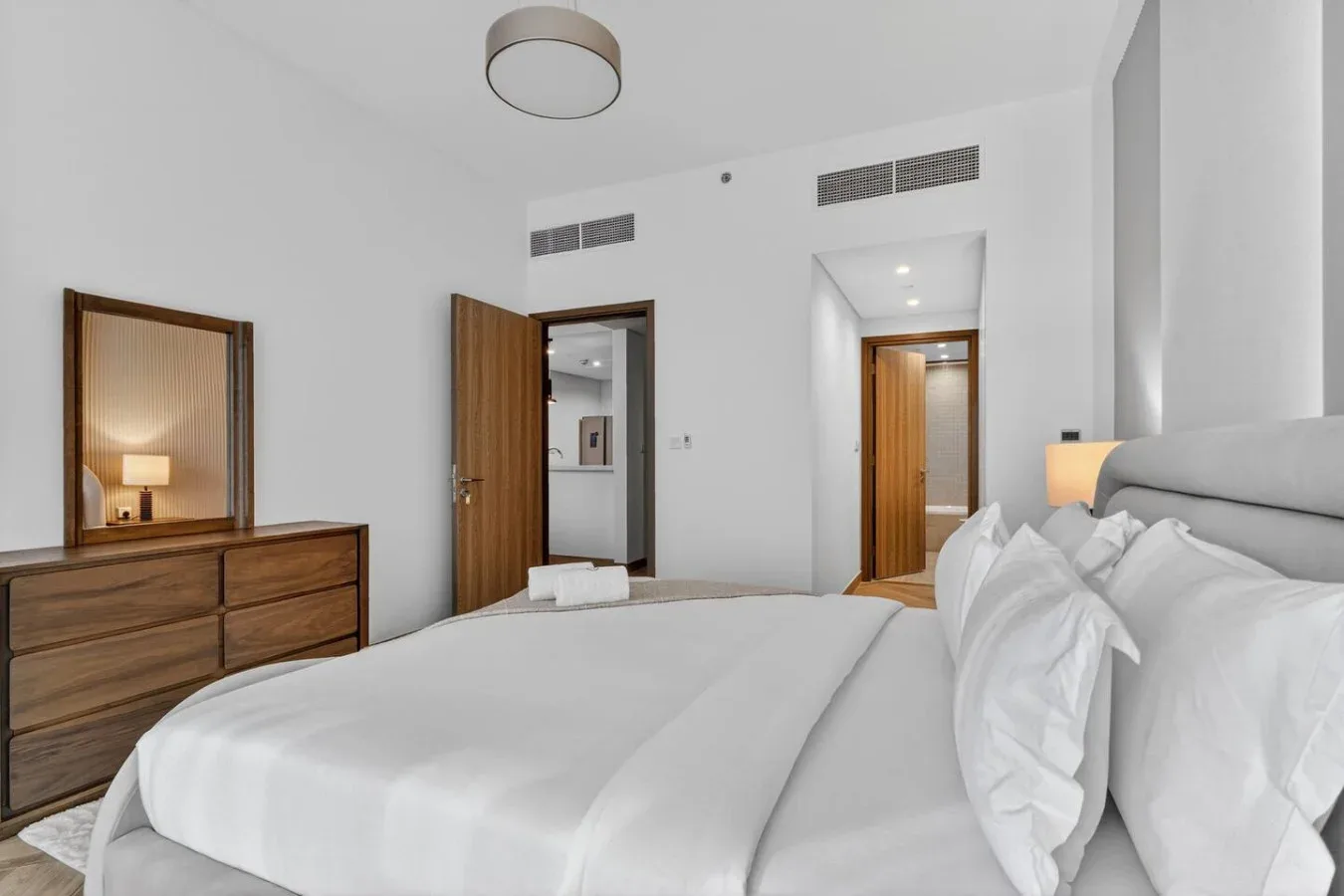 A bright bedroom with a neatly made bed and wooden dresser.