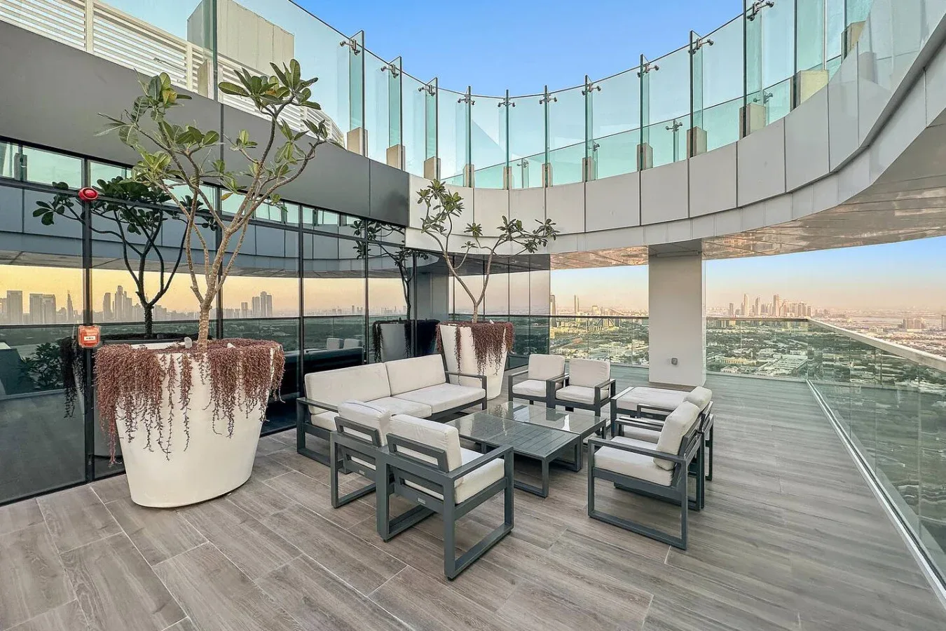 An outdoor terrace with seating, planters, and a glass railing overlooking the city.