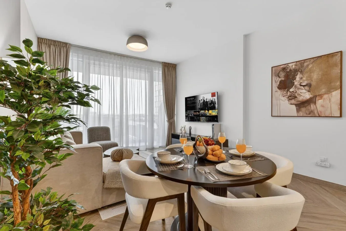 A bright dining and living area features a table set beside large curtained windows.