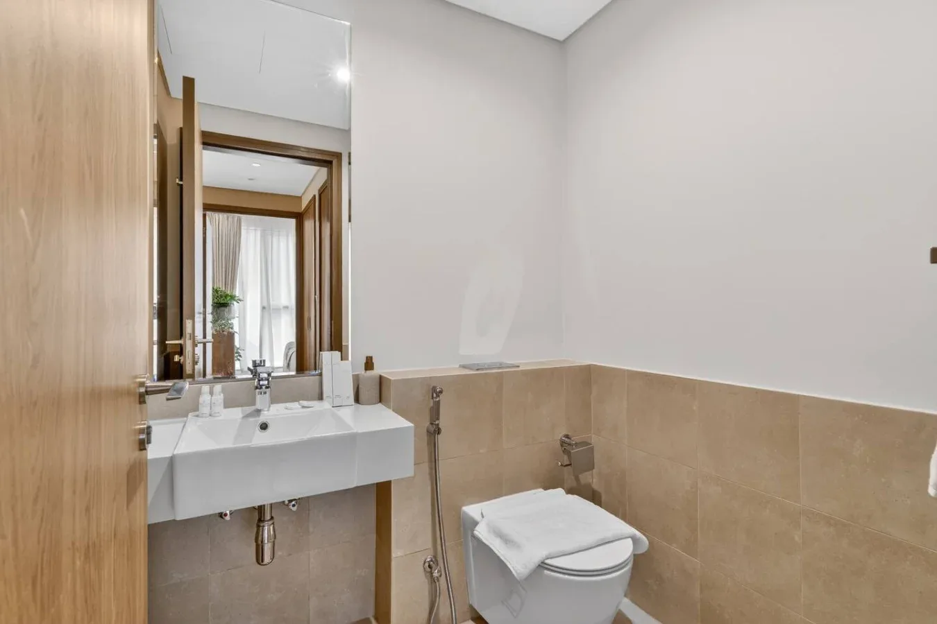 A bathroom with a wall-mounted sink, mirror, and toilet.