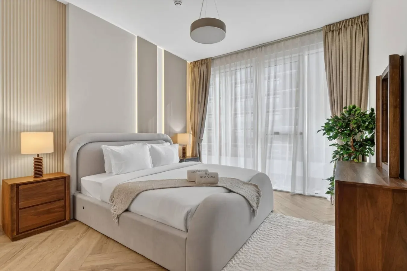 A bedroom with a neatly made bed beside large curtained windows.