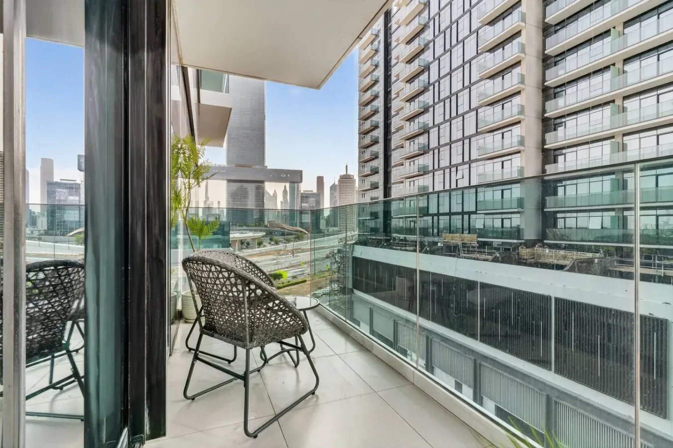 A balcony with woven seating overlooks neighboring modern apartment buildings.