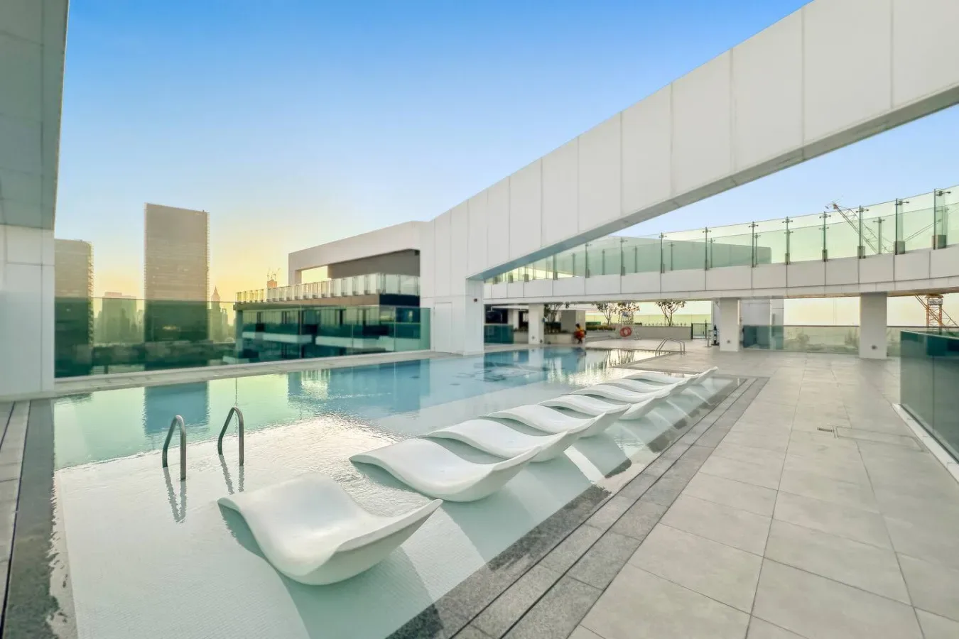 An outdoor swimming pool with sculptural white loungers beside modern buildings.