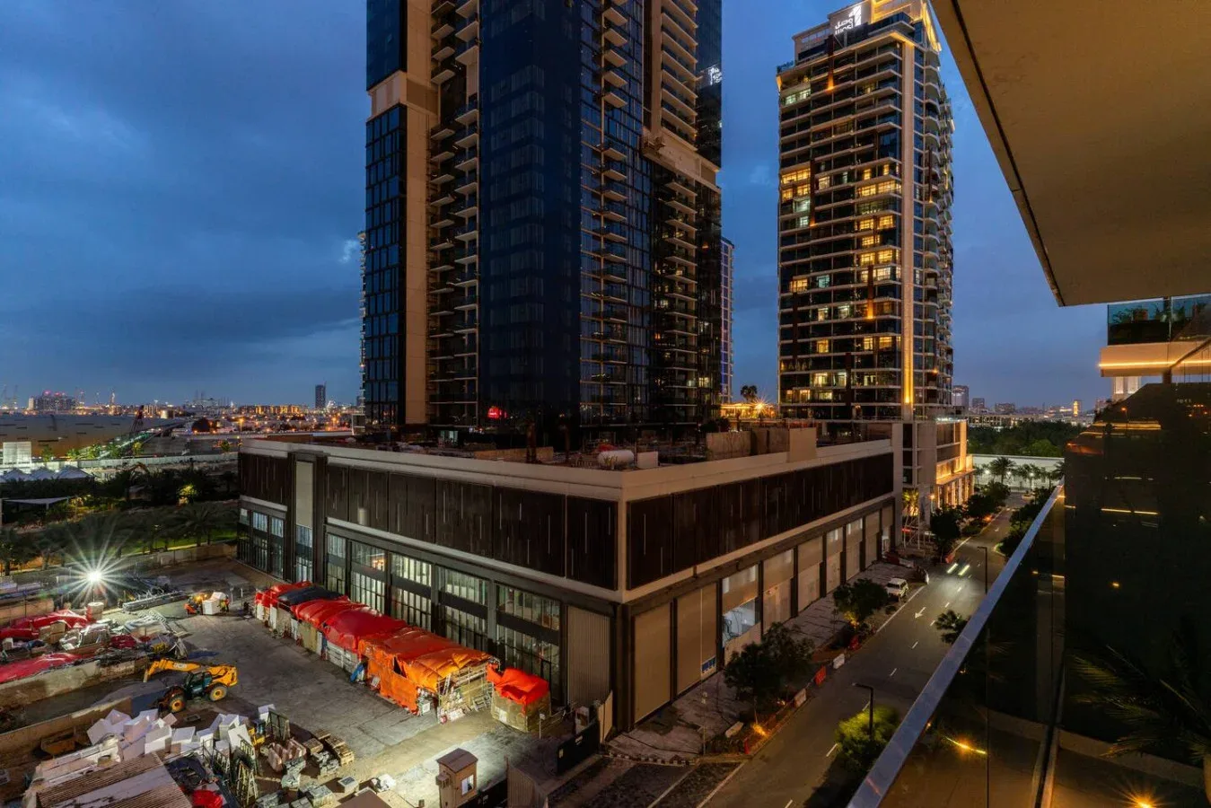 City high-rises overlook a brightly lit construction site at dusk.