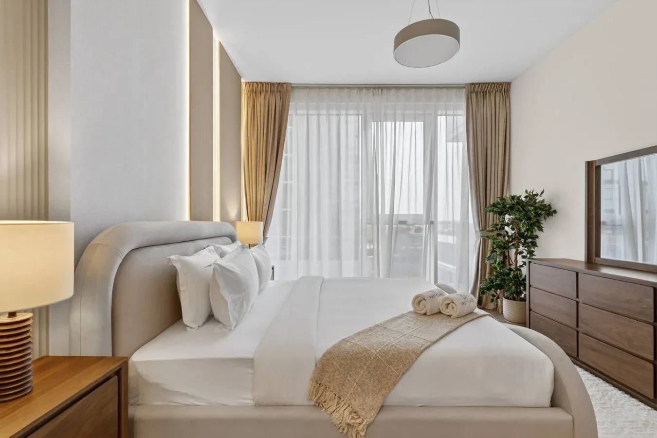 A bright bedroom with a neatly made bed and floor-to-ceiling curtains.