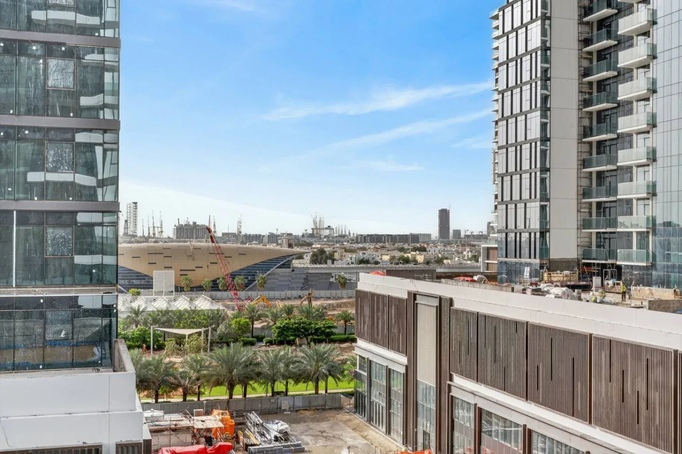 A city view framed by modern buildings, with a landscaped area and construction visible below.