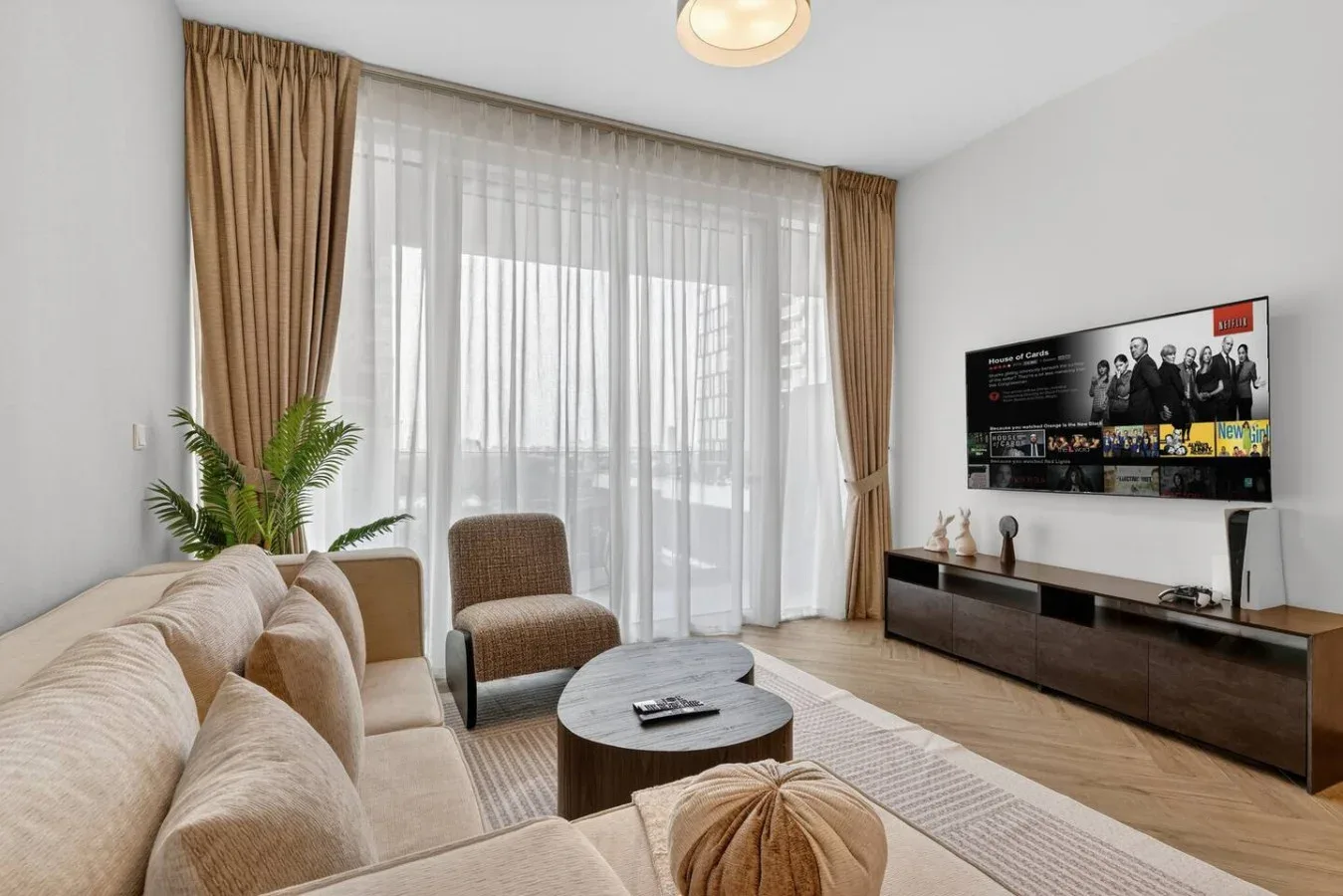 Living room with seating, a coffee table, and a television beside a large curtained window.