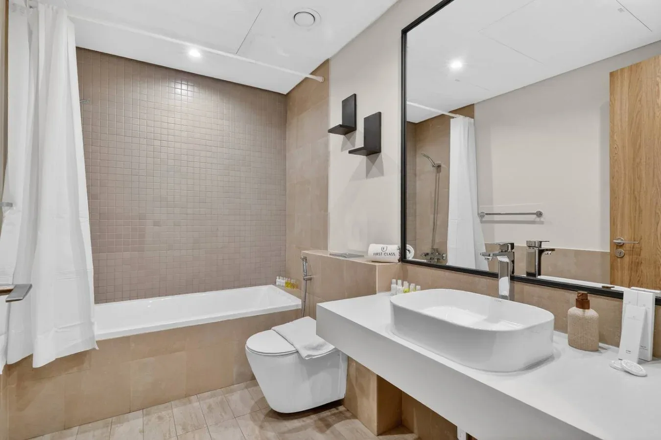 A modern bathroom with a bathtub, toilet, and wide vanity.