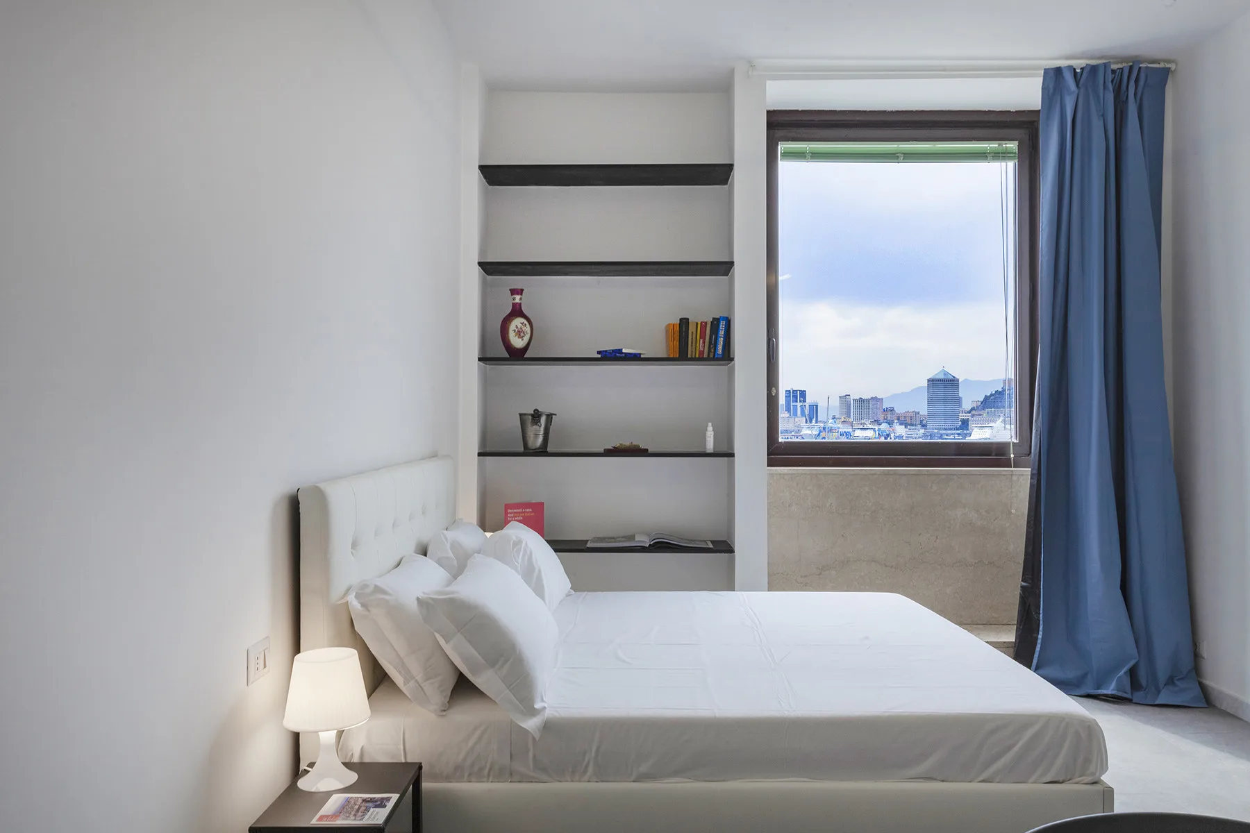 Un dormitorio con una cama bien tendida y una ventana con vistas a la ciudad.