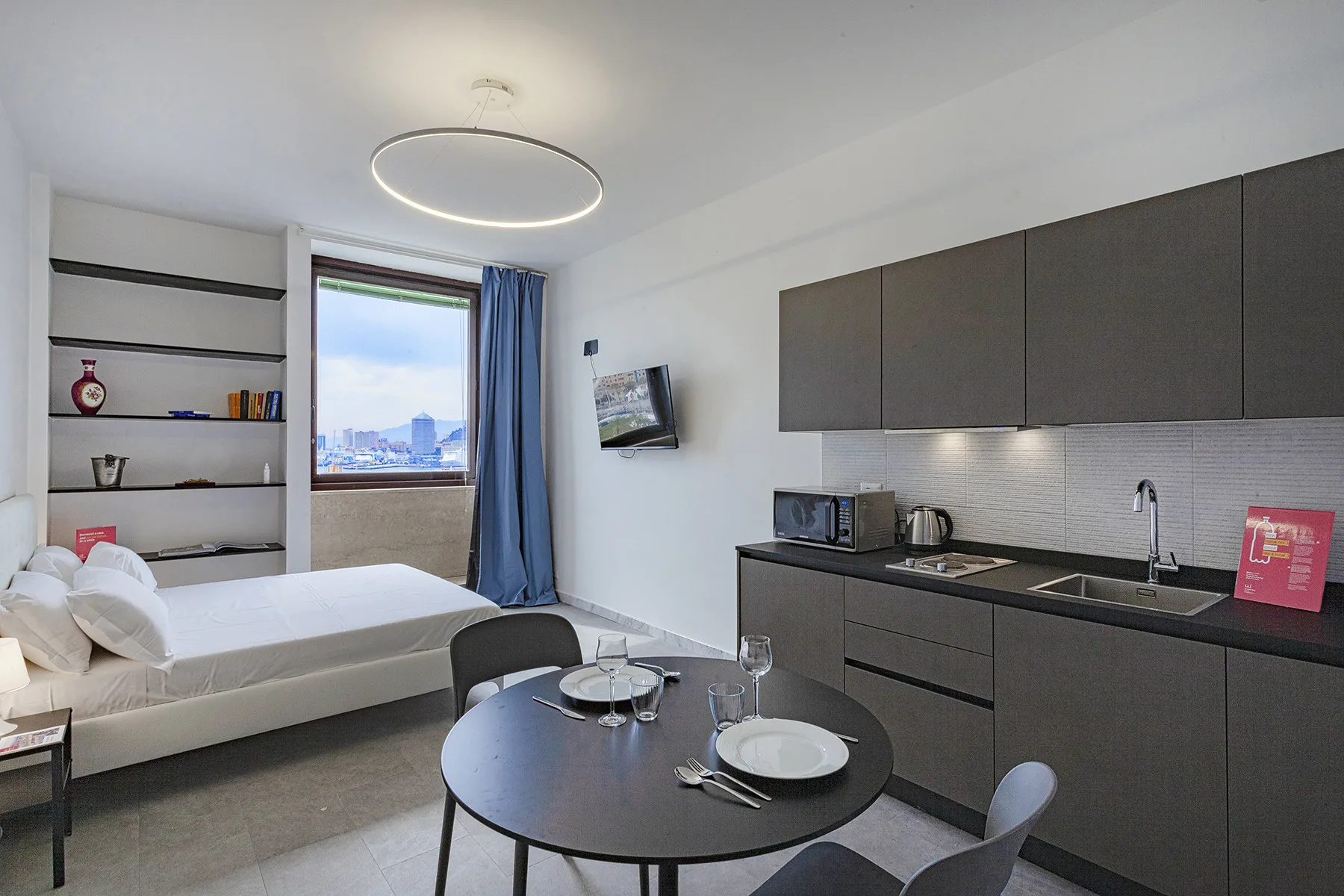 Estudio con cama, cocina pequeña y mesa de comedor redonda.