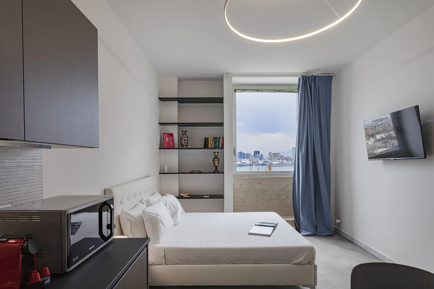 Un dormitorio compacto con cama, estanterías empotradas y una ventana grande.