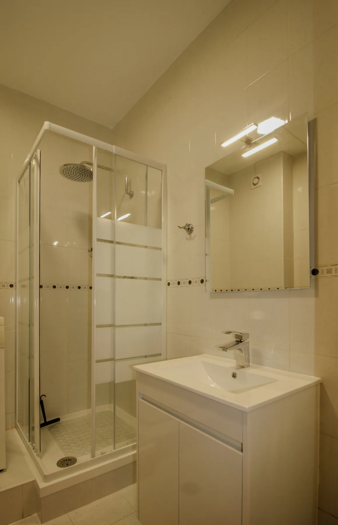 A tiled bathroom with a glass shower and a white sink cabinet.