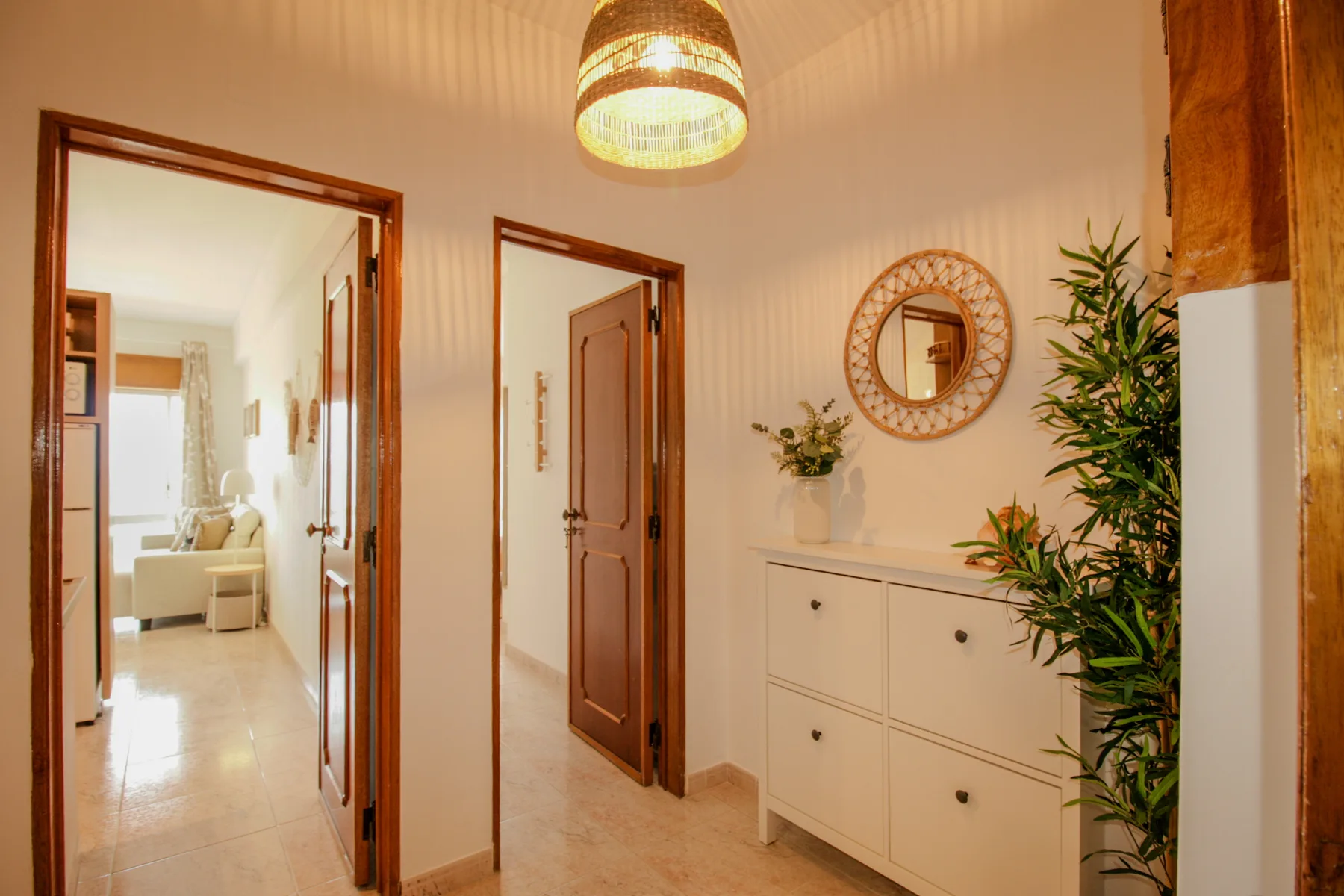 Un recibidor luminoso con un mueble blanco, un espejo redondo y plantas en macetas.