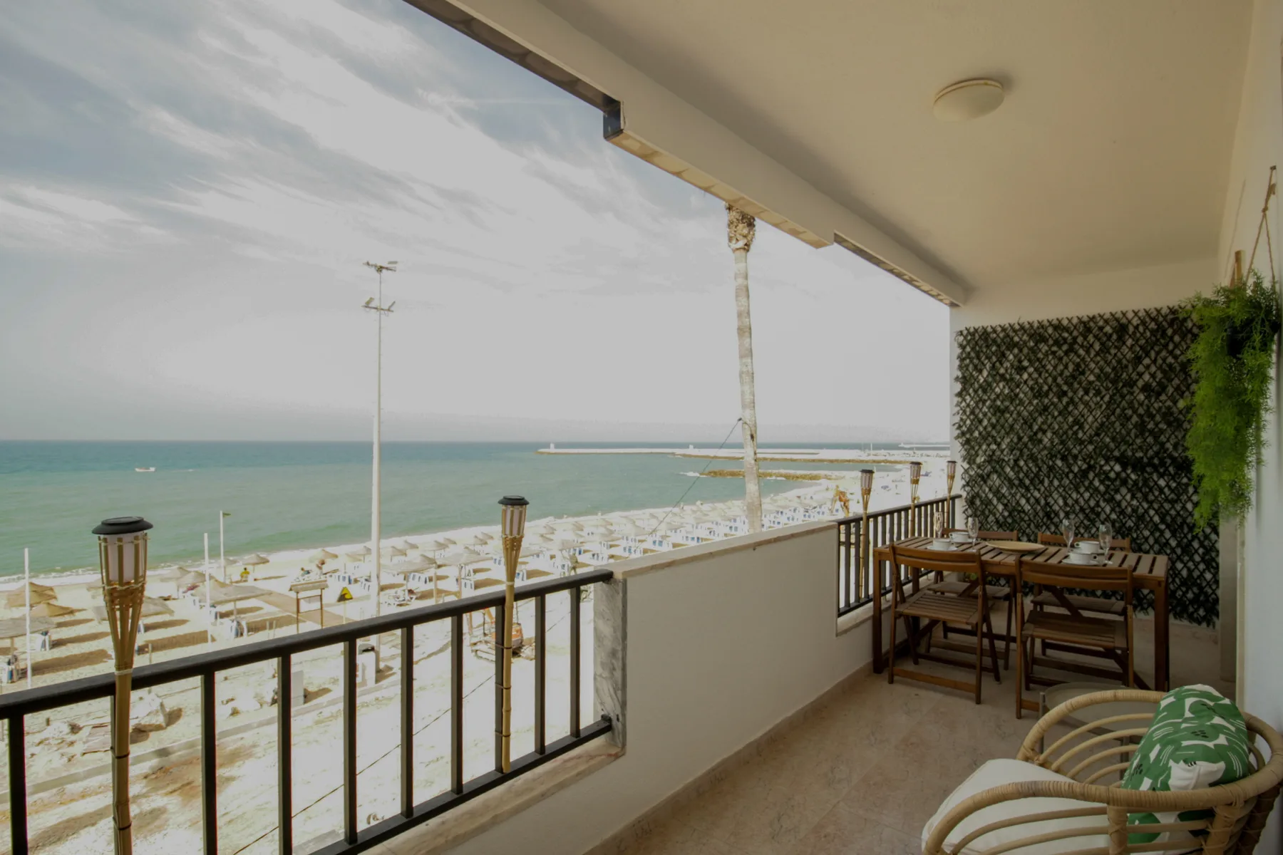 A covered balcony overlooks the beach and sea, with a dining table and chairs.