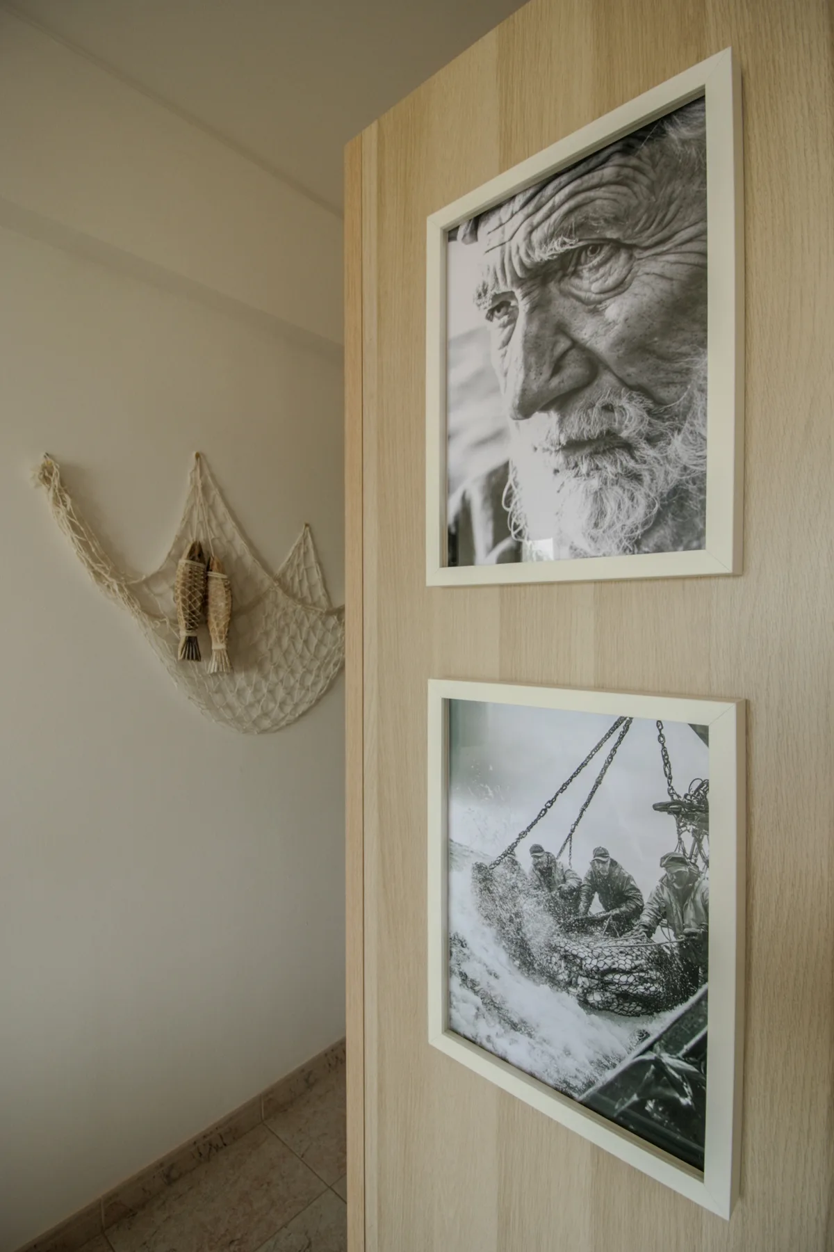 Una pared de pasillo muestra dos fotografías en blanco y negro enmarcadas junto a un adorno tejido.